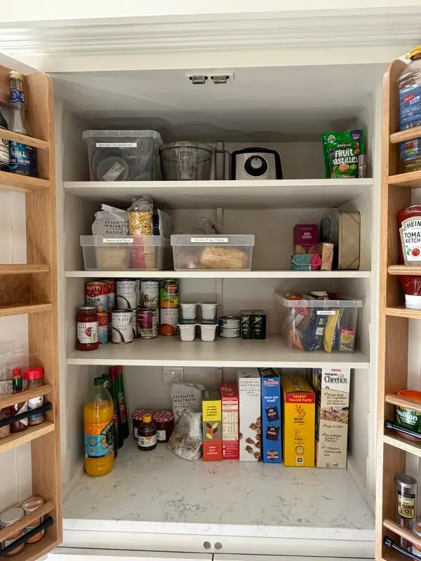 The same pantry cupboard after organising, with labelled clear containers and grouped food categories on each shelf