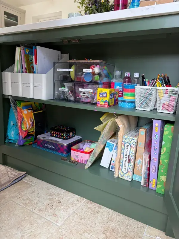 The same craft cupboard after organising, with labelled drawers, file holders and pots for pens and paints