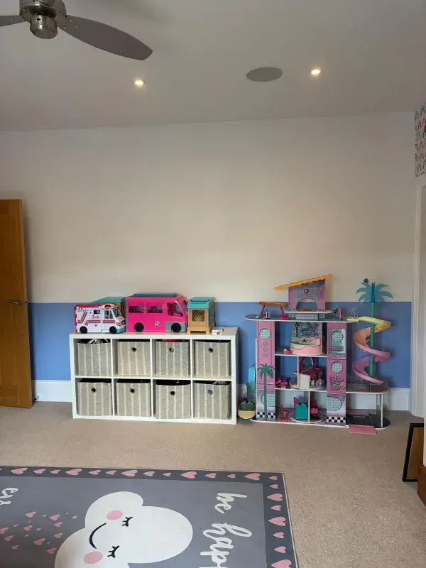 The same playroom after organising, with toys stored in labelled fabric baskets and clear floor space