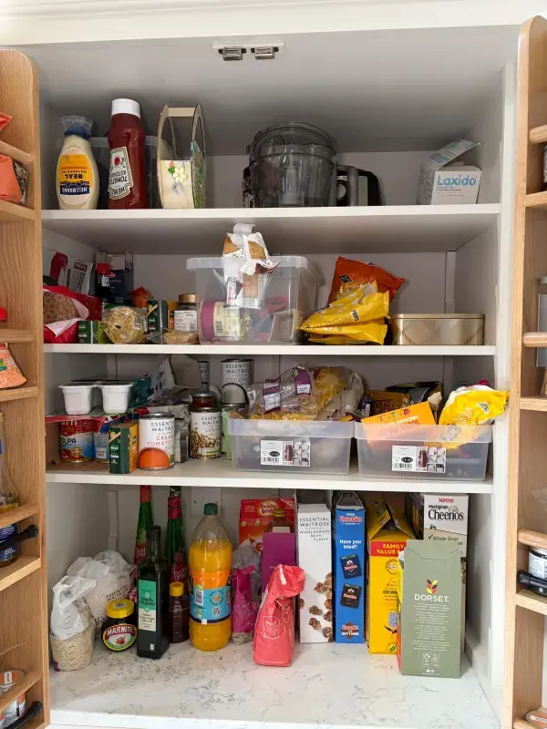 Kitchen pantry cupboard before organising, with food packets and jars stacked loosely across the shelves